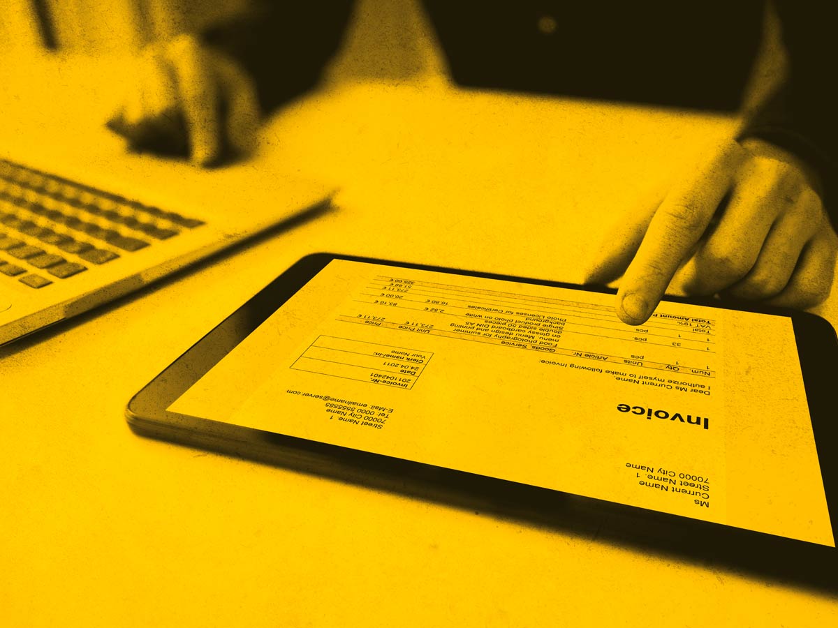 A tablet is on a desk showing an invoice on-screen and a persons finger hovering over the device